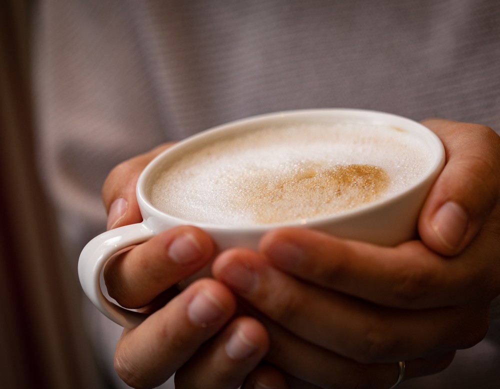 Zwei Hände halten eine große Tasse Milchkaffee.